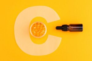Ein großes C mit einem Serum auf orangenem Hintergrund als Symbolbild für den Ratgeber: Vitamin C Serum morgens oder abends?