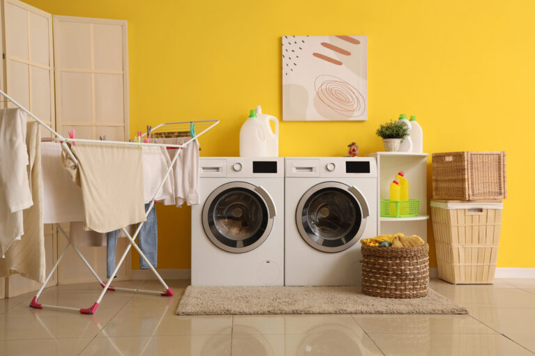 Moderner Wäscheraum mit Trockner, Waschmaschine und Wäscheständer mit Kleidung