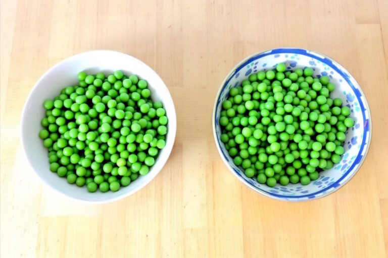 Zwei Schüsseln mit grünen Erbsen nebeneinander, wobei die eine Schüssel 'Erbsen extra fein' und die andere 'Erbsen sehr fein' enthält, um den Unterschied zwischen diesen Erbsensorten zu verdeutlichen.