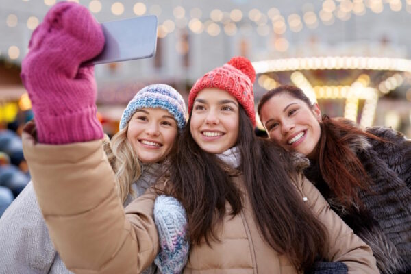 Drei Freunde genießen eine winterliche Auszeit auf einem Weihnachtsmarkt und halten den Moment mit einem Selfie fest – perfekt als Inspiration für gemeinsames Unternehmen in der kalten Jahreszeit.