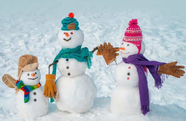 Eine fröhliche Schneemannfamilie mit bunten Accessoires wie Mützen, Schals und Handschuhen stehen im Schnee – eine perfekte Darstellung dafür, was man im Winter mit Kindern unternehmen kann.