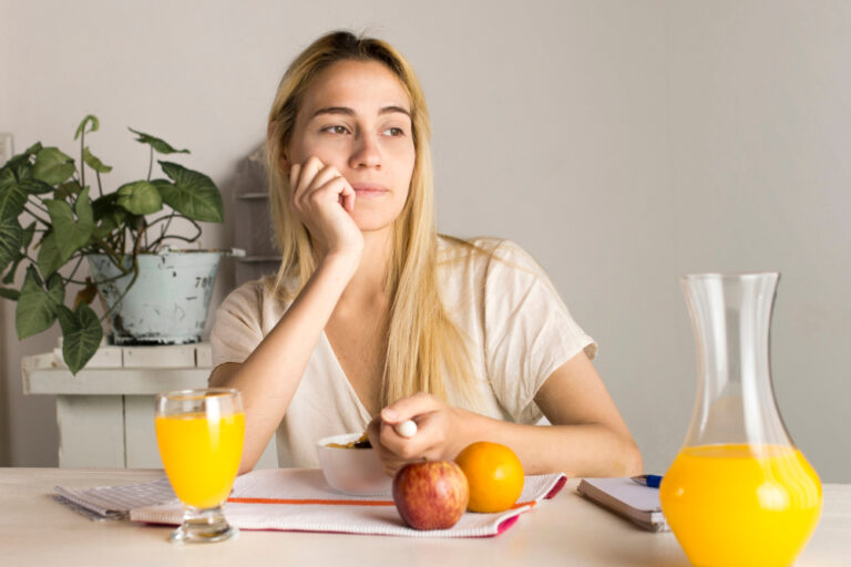 Junge Frau beim Frühstück mit frischem Saft und Obst – Welche Vitamine bei Müdigkeit helfen.