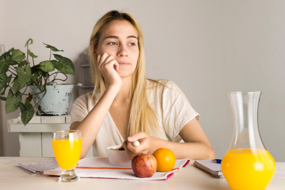 Junge Frau beim Frühstück mit frischem Saft und Obst – Welche Vitamine bei Müdigkeit helfen.