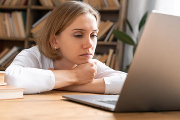 Eine Frau sitzt nachdenklich vor ihrem Laptop, den Kopf auf ihre Hände gestützt. Das Bild symbolisiert das Thema 'Wie kündige ich meinen Job' und spiegelt die Unsicherheit und Überlegungen wider, die oft mit einer beruflichen Kündigung einhergehen.