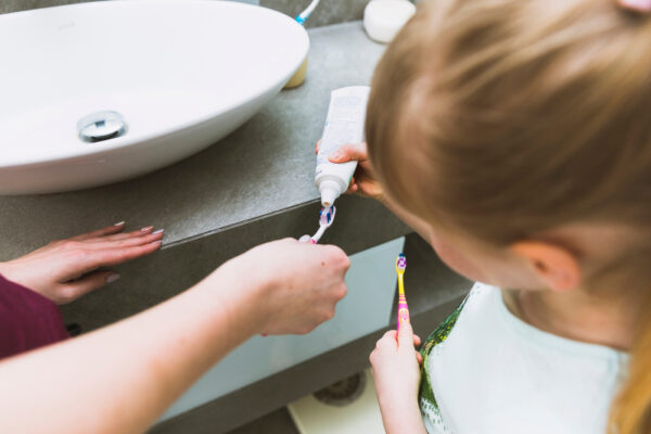 Kind bekommt Zahnpasta auf die Zahnbürste im Badezimmer - bereit machen zum Zähneputzen