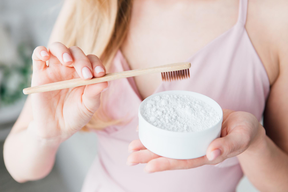 Frau hält eine Bambuszahnbürste und eine Schale mit weißem Zahnpulver.