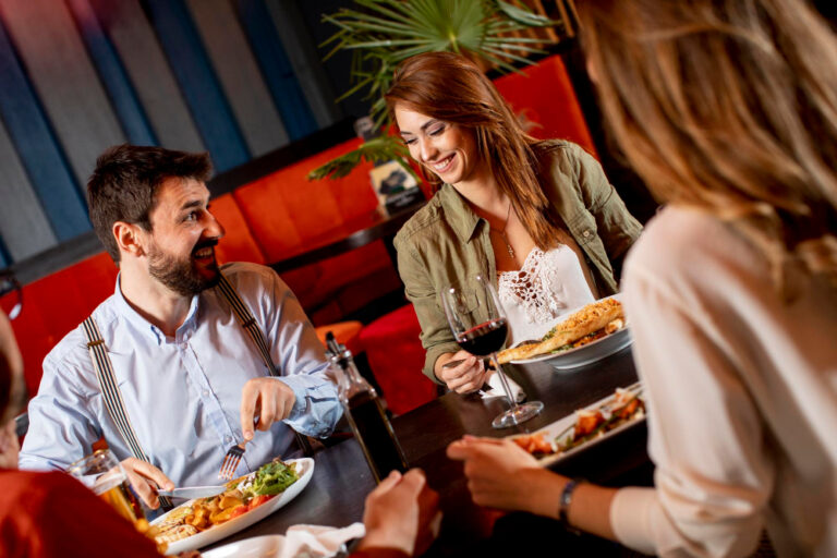 Vier junge Erwachsene essen gemeinsam in einem Restaurant und lachen.