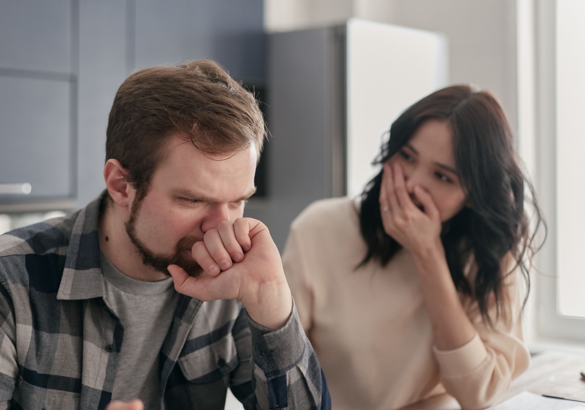 Ein Mann hält sich die Hand vor Nase und Mund, während eine Frau neben ihm ebenfalls den Mund bedeckt.