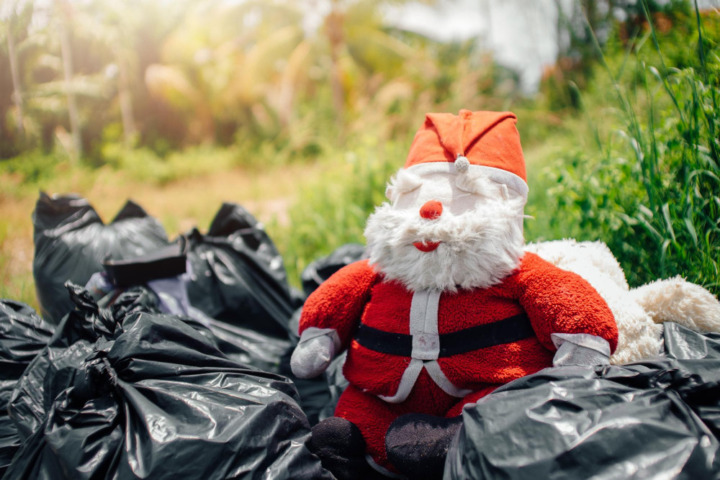 Stoff-Weihnachtsmann sitzt zwischen mehreren schwarzen Müllsäcken im Freien