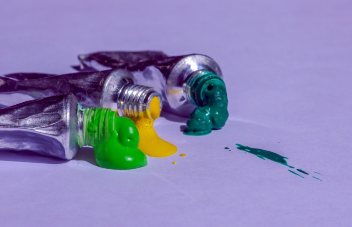Drei offene Farbtuben mit grüner, gelber und türkisfarbener Farbe liegen auf einer hellen Fläche; etwas Farbe ist ausgelaufen.