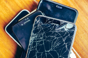 Alte Handys entsorgen: Mehrere ausrangierte Smartphones liegen übereinander, eines mit gesprungenem Display als Symbol für Elektroschrott und Recycling.