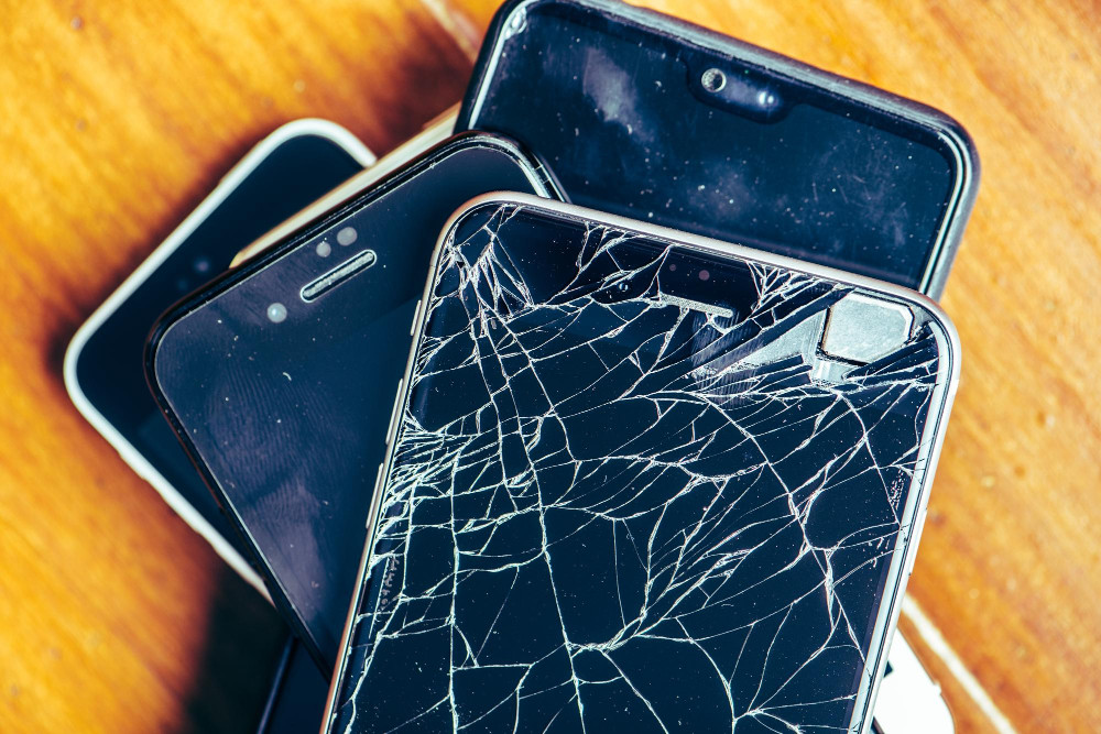 Alte Handys entsorgen: Mehrere ausrangierte Smartphones liegen übereinander, eines mit gesprungenem Display als Symbol für Elektroschrott und Recycling.