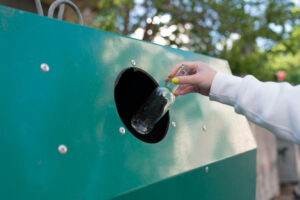 Altglas entsorgen: Hand wirft eine leere Glasflasche in den Altglascontainer.