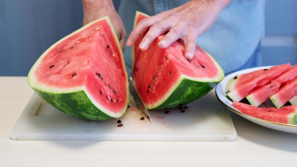 Angeschnittene Wassermelone auf einem Schneidebrett mit Melonenspalten auf einem Teller