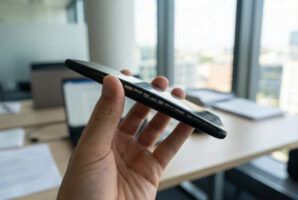 Seitenansicht eines Smartphones mit gefährlich aufgeblähtem Akku in einer Hand vor einem unscharfen Büro-Hintergrund.