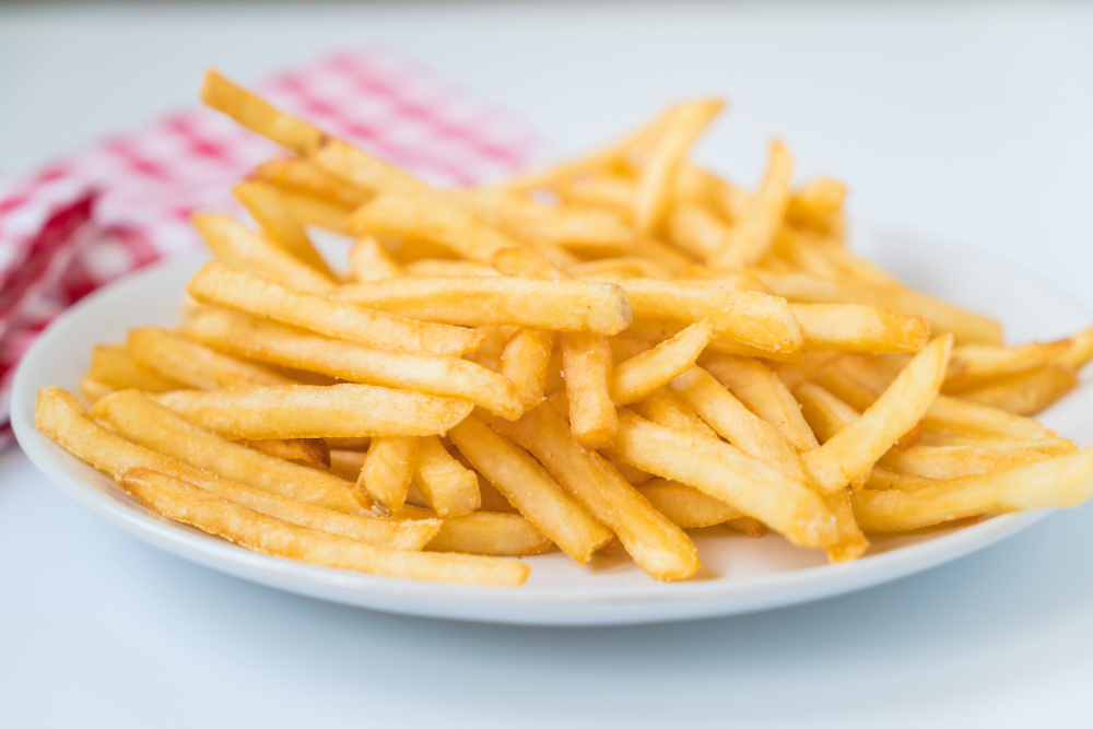 Goldgelbe, knusprige Pommes frites auf einem weißen Teller vor kariertem Stoff.