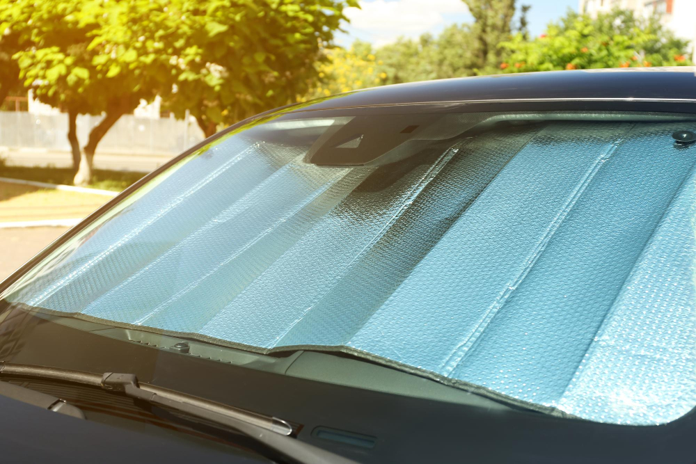 Reflektierende Sonnenblende hinter der Windschutzscheibe eines geparkten Autos schützt den Innenraum im Sommer vor direkter Sonne.