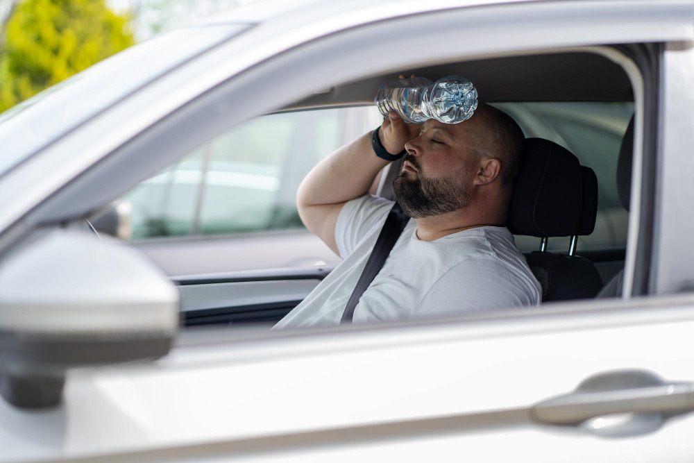 Mann im heißen Auto kühlt sich mit einer Wasserflasche an der Stirn