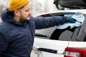 Mann trocknet das Heck eines weißen SUV mit Mikrofasertuch, um Lack und Dichtungen vor Salz und Frost in Winter zu schützen.