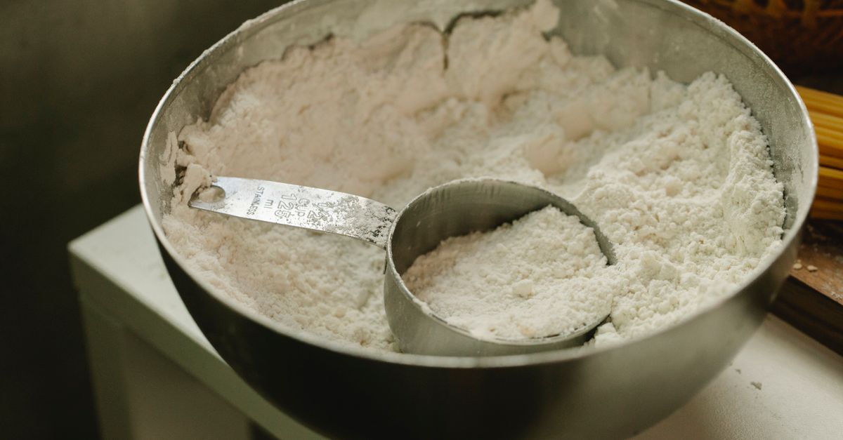 From above of round shaped metal bowl with flour and measuring cup at home