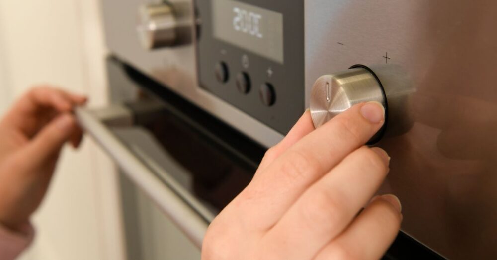 Hand dreht den Temperaturregler eines eingebauten Backofens