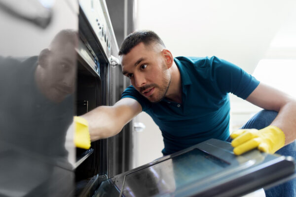 Person reinigt den Innenraum eines geöffneten Backofens mit einem weichen Schwamm