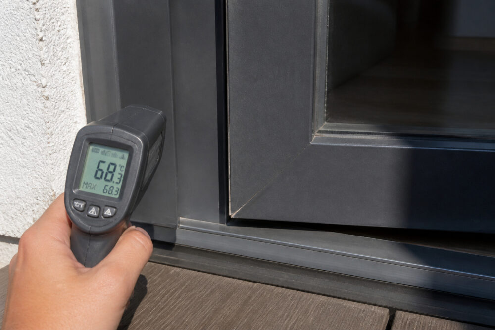 Infrarotthermometer misst hohe Temperatur an einer dunklen Balkontür in direkter Sonne