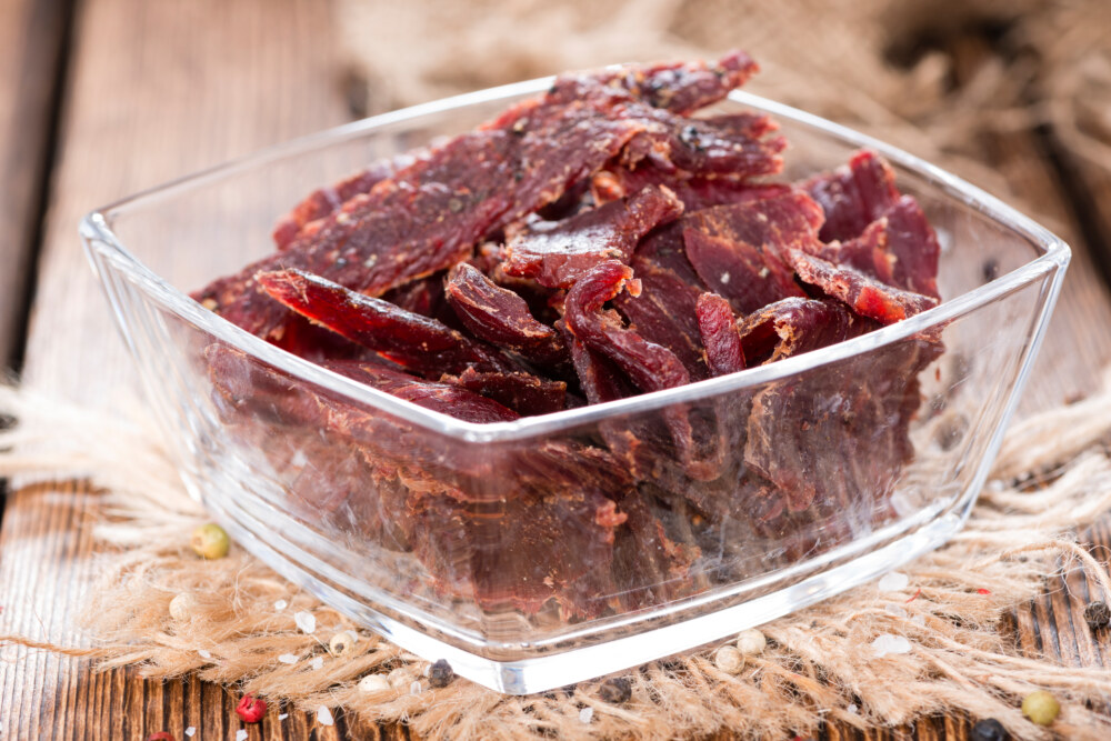 In einer quadratischen Glasschale liegen dunkelrotbraune, unregelmäßig geformte Streifen Beef Jerky.