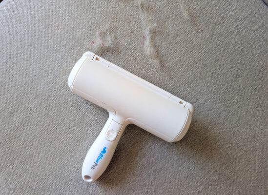 BluePet RolloTollo Tierhaarentferner auf grauem Sofa neben aufgenommenen Tierhaaren