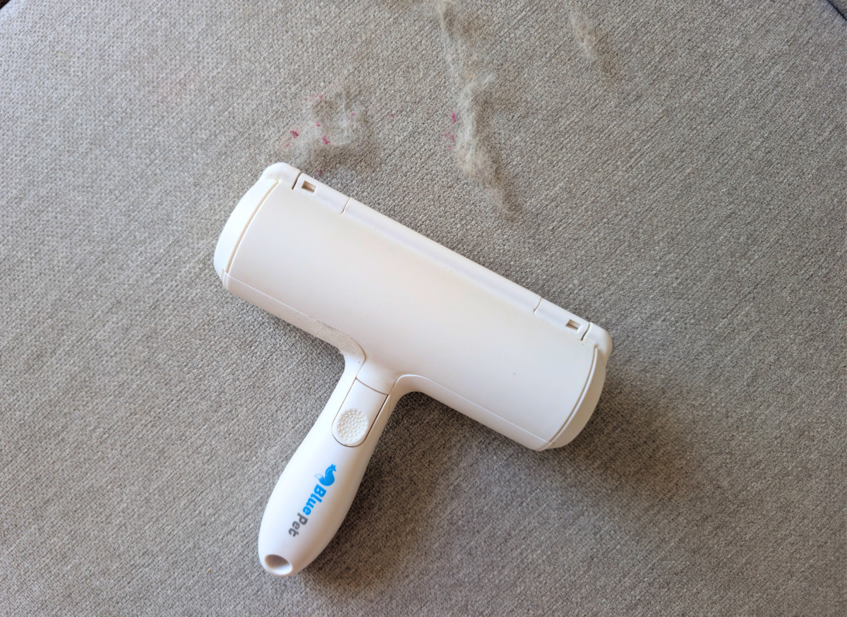 BluePet RolloTollo Tierhaarentferner auf grauem Sofa neben aufgenommenen Tierhaaren