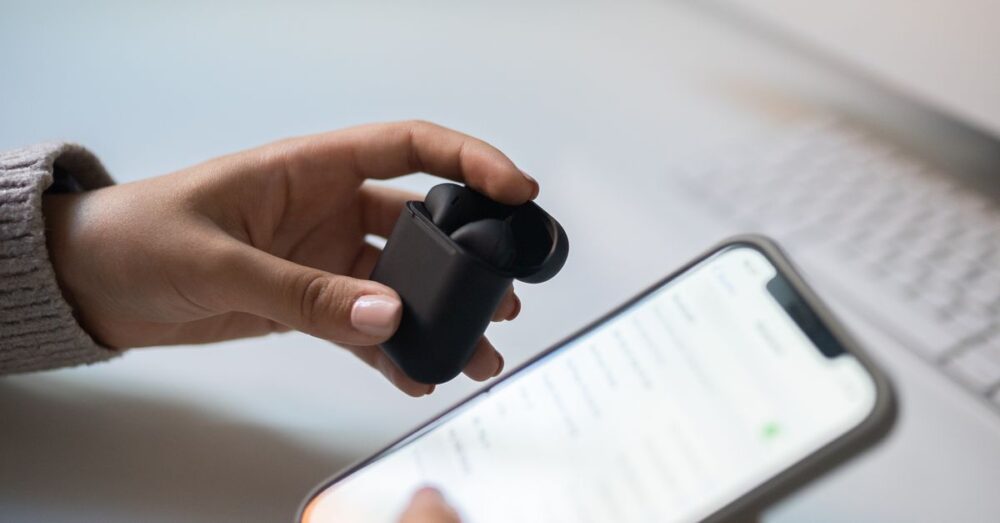 Hand hält kabellose In-Ear-Kopfhörer neben einem Smartphone mit geöffneten Bluetooth-Einstellungen