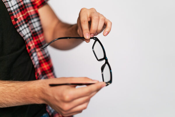 Person hält eine schwarze Brille in beiden Händen und betrachtet die Gläser