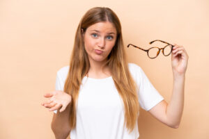 Frau mit fragendem Blick hält Brille in der Hand