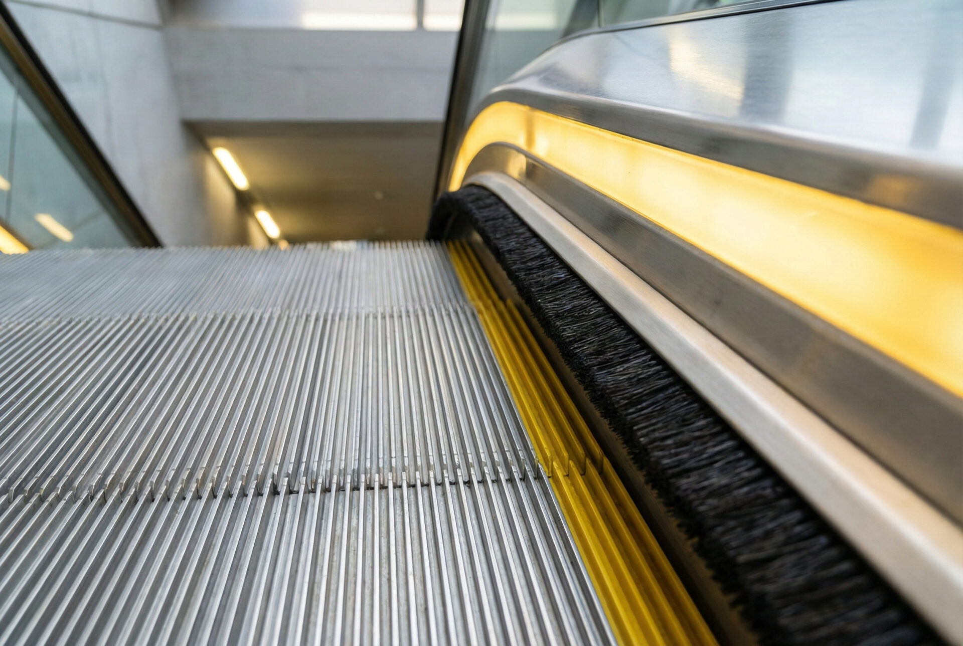 Bürsten an der Rolltreppe am Seitenrand: Nahaufnahme von Stufe, gelber Markierung und Sockelbürste, die Abstand zum Spalt zwischen Stufe und Seitenwand schafft.