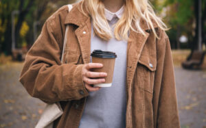 Person hält Coffee-to-go-Becher unterwegs in der Hand