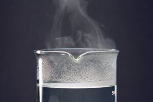 Dampfendes Wasser in einem Becherglas als Ausgangspunkt für die Gewinnung von destilliertem Wasser.