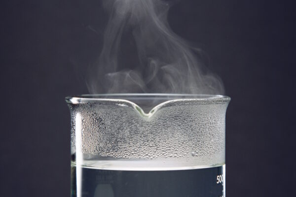 Dampfendes Wasser in einem Becherglas als Ausgangspunkt für die Gewinnung von destilliertem Wasser.