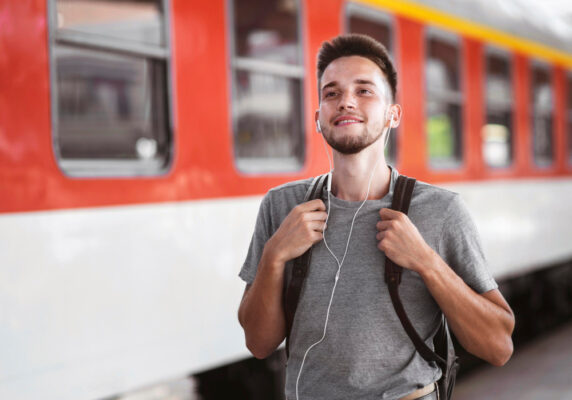 Junger Mann mit Rucksack und Kopfhörern am Bahnhof vor einem Regionalzug - Deutschlandticket für 63 Euro im Alltag