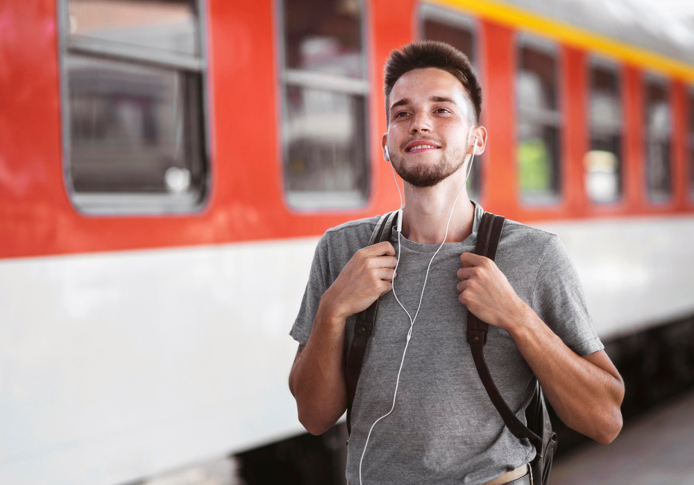 Junger Mann mit Rucksack und Kopfhörern am Bahnhof vor einem Regionalzug - Deutschlandticket für 63 Euro im Alltag
