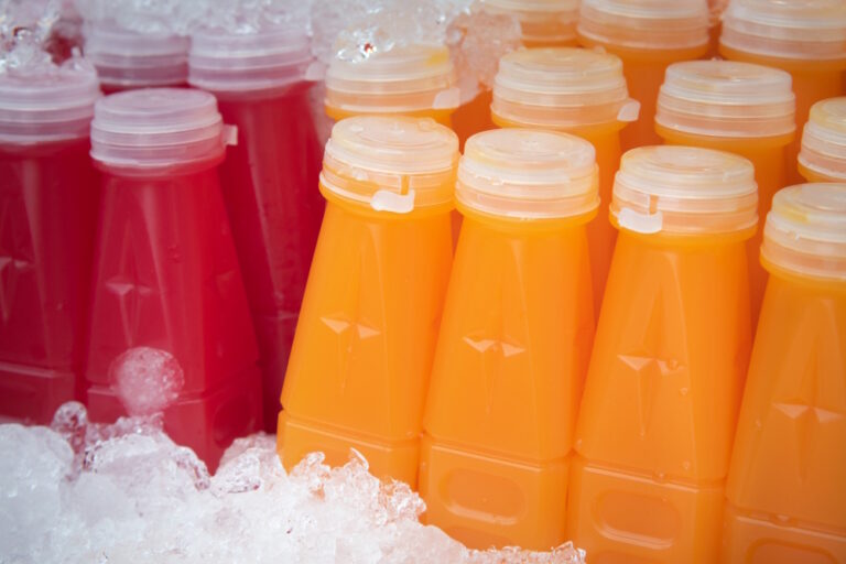 Plastikflaschen mit orangefarbenem und rotem Fruchtsaft liegen in Eis