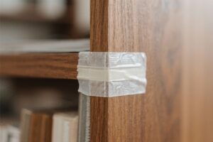 Altes, sprödes Klebeband an der Ecke eines Holzregals – Beispiel für hartnäckige Klebebandreste auf Holz vor dem Entfernen