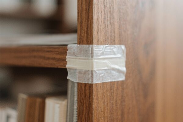 Altes, sprödes Klebeband an der Ecke eines Holzregals – Beispiel für hartnäckige Klebebandreste auf Holz vor dem Entfernen