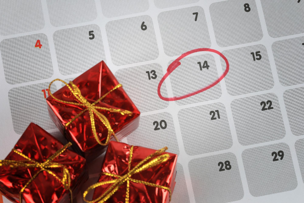 Der 14. Dezember im Kalender ist eingekreist, drumherum liegen 3 in rote Folie verpackte Geschenke (Symbolfoto für Datum der Weihnachtsfeier)