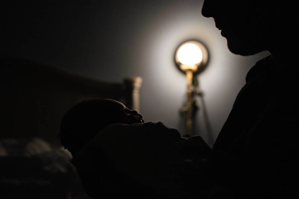 Ein Baby wird liebevoll von einem Erwachsenen im abgedunkelten Raum gehalten, mit sanftem Licht im Hintergrund – symbolisch für Einschlaftipps und beruhigende Rituale für Babys.