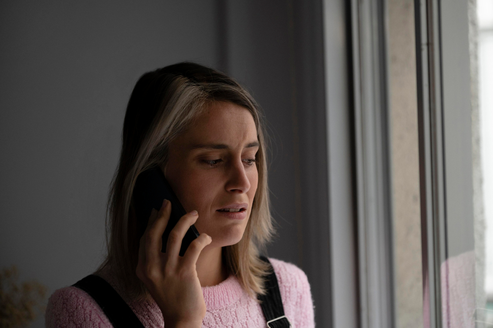 Eine Frau telefoniert besorgt am Fenster, weil ihr Partner im Gespräch mitteilt, dass er sich in eine andere verliebt hat.