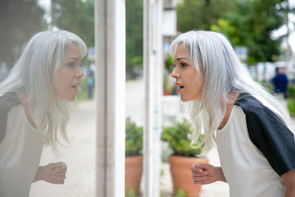 Frau mit grauen Haaren blickt erschrocken in ein spiegelndes Fenster