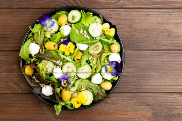 Grüner Salat mit Gurke, Oliven, Käse und violetten sowie gelben Stiefmütterchen