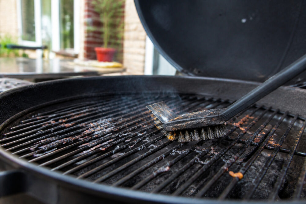 Verkohlte Essensreste auf einem Grillrost werden mit einer Bürste entfernt