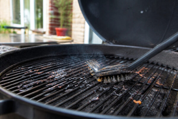 Verkohlte Essensreste auf einem Grillrost werden mit einer Bürste entfernt