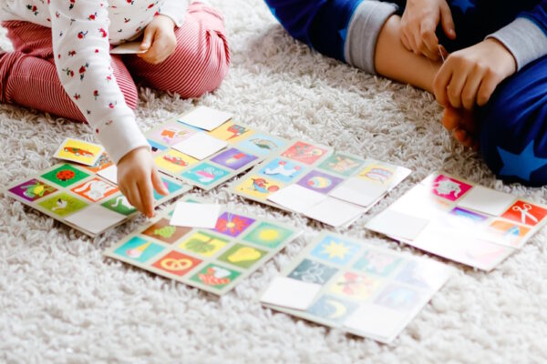 Kinder spielen ein Memory-Spiel mit bunten Karten auf einem Teppich, eine Aktivität, die das fotografische Gedächtnis trainieren kann.